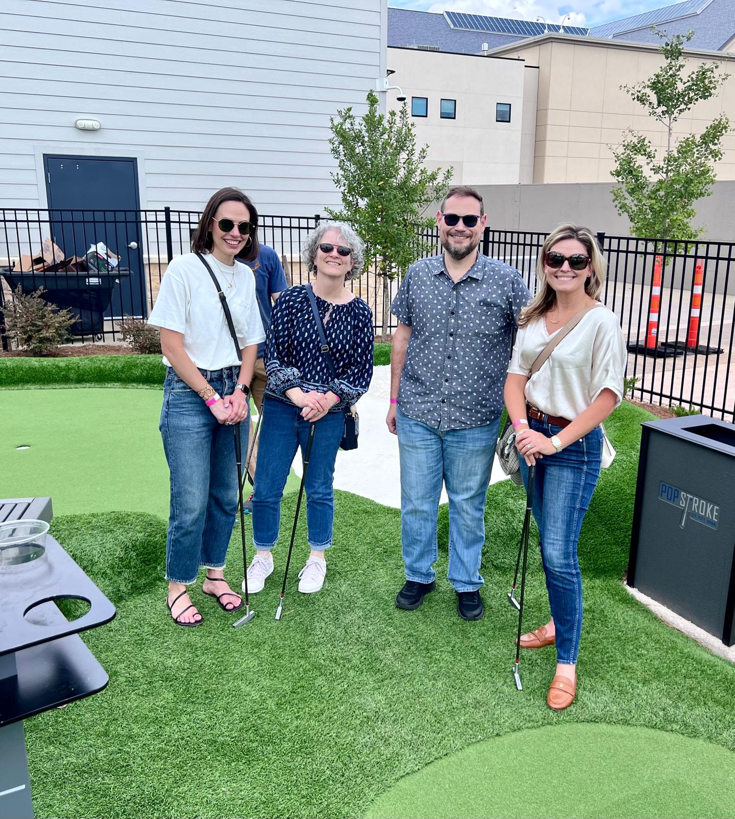 a group of people standing on a green field with golf clubs